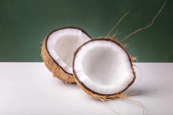 茶色の外殻と白いココの内部が暗い緑色の背景に対して白い表面にココナッツの2つの半分 — ストック写真