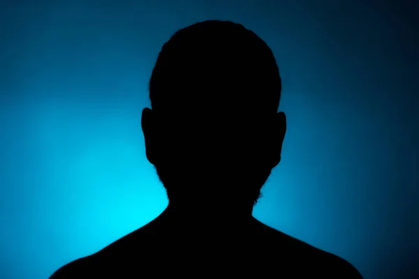 Cleanly defined frontal silhouette of a male person against a blue background with a spotlight and bright area right behind the bust. Studio shot with well defined explicit colour background.