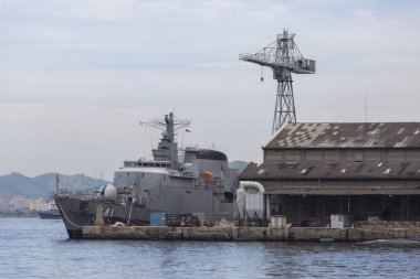 Rio de Janeiro Guanabara koyunda deniz adası Ilha das Cobras üzerinde mavi gökyüzü ve dramatik bulutlar yukarıda güneşli bir günde bir vinç yanında demirlemiş büyük bir savaş gemisi ile görünümü