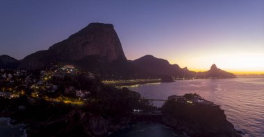 Arka planda Gavea, Vidigal ve Corcovado dağları ve şafakvakti sokak ışıkları ve yoğun sabah renkleri ile ön planda Costa Brava kulübü ile Joatinga plajı havadan görünümü