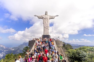 Rio de Janeiro, Brezilya - 13 Temmuz 2017: Rio de Janeiro'daki Corcovado dağının tepesinde, üzerinde yükselen İsa heykeli ve mavi gökyüzünde dramatik bulutlar ile turist kalabalığı