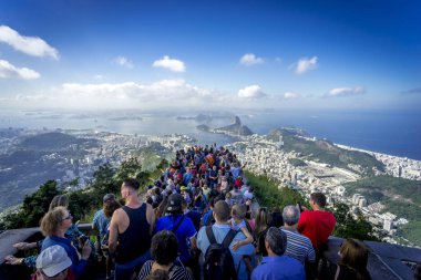Rio de Janeiro, Brezilya - 13 Temmuz 2017: Mavi gökyüzü ve bulutların olduğu parlak güneşli bir günde Rio de Janeiro'nun ikonik manzarasına bakan Corcovado dağının tepesindeki turist kalabalığı