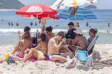 Rio de Janeiro, Brezilya - 30 Ocak 2016: Sıcak bir yaz gününde arka planda suda olan insanlarla gölgede bir araya gelen plaj müdavimleri