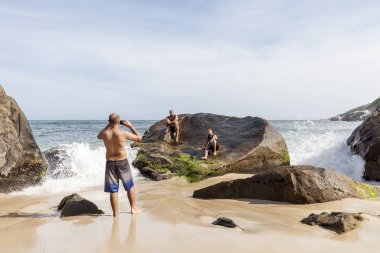Rio de Janeiro, Brezilya - 30 Ocak 2016: Kayalara çarpan dalgaların olduğu bir plajda insanlar doğru anı sabırla telefonla poz ve fotoğraf çekiyorlar