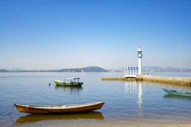 Mavi su ve mavi gökyüzü ile Rio de Janeiro Guanabara koyunda Paqueta tropikal adada küçük deniz feneri ile tekneler ve iskele