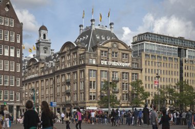 Amsterdam, Hollanda - 24 Ağustos 2012: Amsterdam'ın merkez meydanında, ön planda insanlar ve güvercinlerle birlikte De Bijenkorf'un tarihi pazar binası
