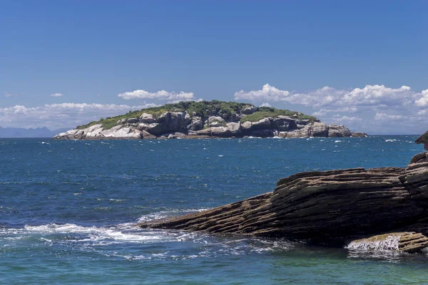 Coastline of popular holiday destination Buzios in Rio de Janeiro, Brazil, with an island in the background against a clear blue sky with clouds in the distance