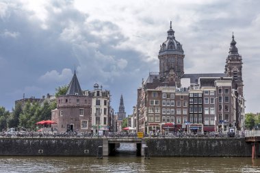 Amsterdam, Hollanda - 24 Ağustos 2012: Bulutlu bir günde bir kule ve tipik kanal evleri ve bir kilise ile Amsterdam şehir merkezinde kanal görünümü