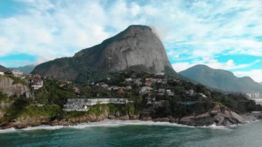 Aerial approach of the beautiful picturesque cliff rocks of Joatinga beach in Rio de Janeiro with the Gavea mountain towering behind it and the green ocean waves rolling in