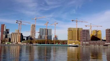 Financial district of Rotterdam on the shore of the broad river with modern buildings and construction cranes revealing a subway train passing on a viaduct above street level