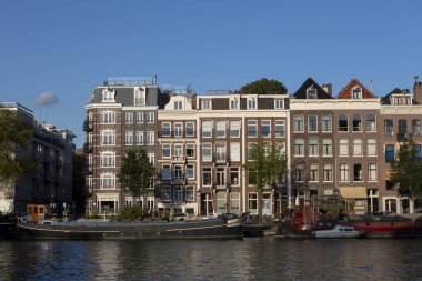 Amsterdam, Hollanda - 2 Eylül 2019: Günbatımında seyyar su tekneleriyle Amsterdam kanalı şehir manzarası