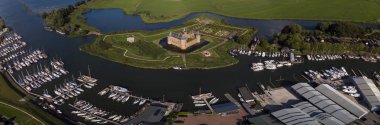 Amsterdam yakınlarındaki Muiden 'daki Muiderslot şatosu ve Ijsselmeer' deki yemyeşil bahçeleri ile birlikte gün batımında etrafındaki su siperleri ile adanın panoramik manzarası.