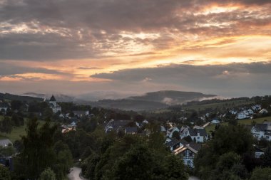 Almanya 'nın Sauerland kentindeki kış sporları bölgesindeki Grafschaft adlı dağlık spa köyünün günbatımı boyunca renkli bir gökyüzü ile panoramik manzarası