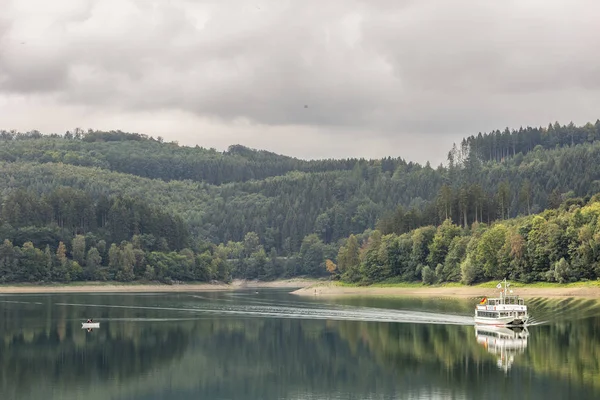 Sauerland bölgesindeki Alman Hennesee Gölü 'nden geçen zevk teknesi bir iz bırakıyor ve bulutlu bir günde durgun suya yansıyor.