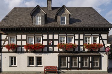 Almanya 'nın Sauerland bölgesindeki Grafschaft adlı spa köyündeki tipik yarı keresteli Vakwerk evinin mimarisi. Çiçekler mavi gökyüzüne karşı bulutlarla süsleme yapıyor.