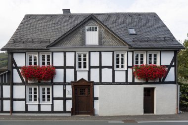Almanya 'nın Sauerland bölgesindeki Grafschaft adlı spa köyündeki tipik yarı keresteli Vakwerk evinin mimarisi ön cepheyi kırmızı çiçeklerle süslüyor.
