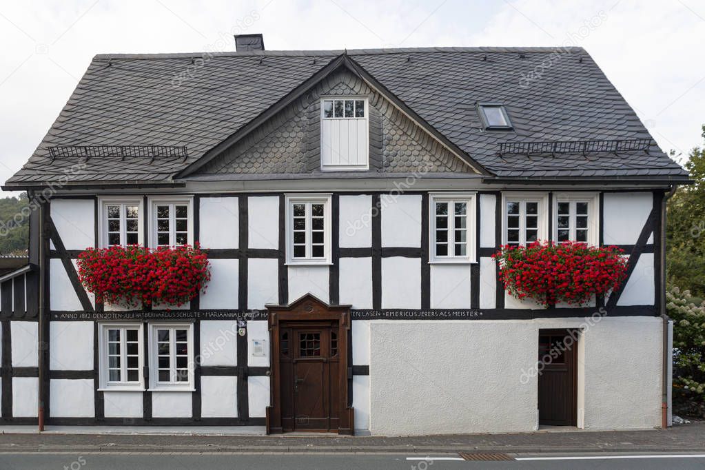 Architecture of typical half-timbered Vakwerk home in the spa village of Grafschaft in the Sauerland region in Germany with red flowers decorating the facade