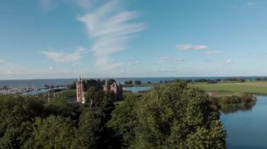 Aerial reveal of the Muiderslot castle in Muiden near Amsterdam and its lush gardens at the IJsselmeer with surrounding water entrenchment in the foreground