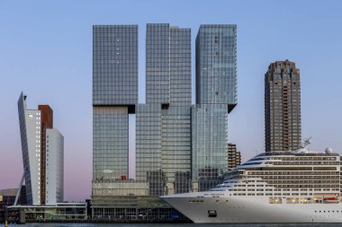 Rotterdam 'ın Hollanda liman kenti gökdelenleri önünde gün batımında finans bölgesi gökdelenleri olan bir yolcu gemisi.