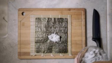 Ahşap kaşık ve mutfak tezgahında tablet keserek paspasa çay tohumu ve suşi yapmak için yosun ve Norveç çarşafı serpiştirilmiş pirinç serpiştirilmiş.