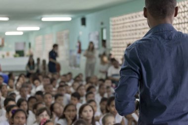 Rio de Janeiro, Brezilya - 2 Temmuz 2015: Odaklı öğretmen odak noktasından bakıldığında odak dışı bir sınıf dolusu okul üniformalı öğrencinin yerde oturduğunu bulanıklaştırdı 