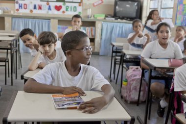 Rio de Janeiro, Brezilya - 2 Temmuz 2015: Okul üniformalı okul çocuğu masasında oturmuş, sınıf ve sınıf arkadaşlarının dikkatine arka planda bakıyor.