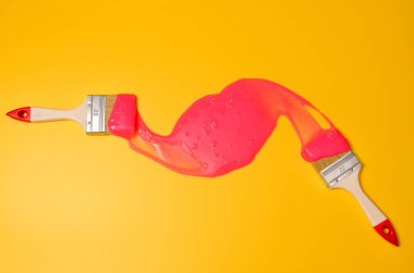 Sarı arka planda pembe yapışkan sümüklü fırça. Fotoğrafçılıkta minimalizm, konsept yaratıcı resim. Boyama aracı