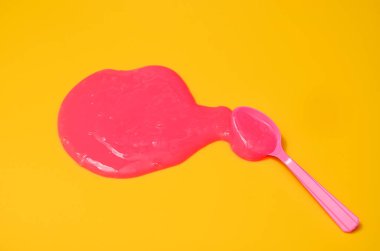 Sarı arka planda pembe yapışkan sümüklü klasik mavi kaşık. Fotoğrafçılıkta minimalizm, konsept yaratıcı resim. Boyama aracı