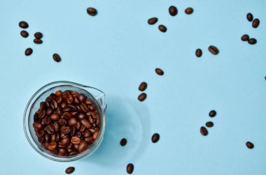 Kahve çekirdekleri nane mavisi arka planda kristal bir kavanozdan dökülüyor. Pastel renkli duvar kağıdı, moda fotoğrafçılığı