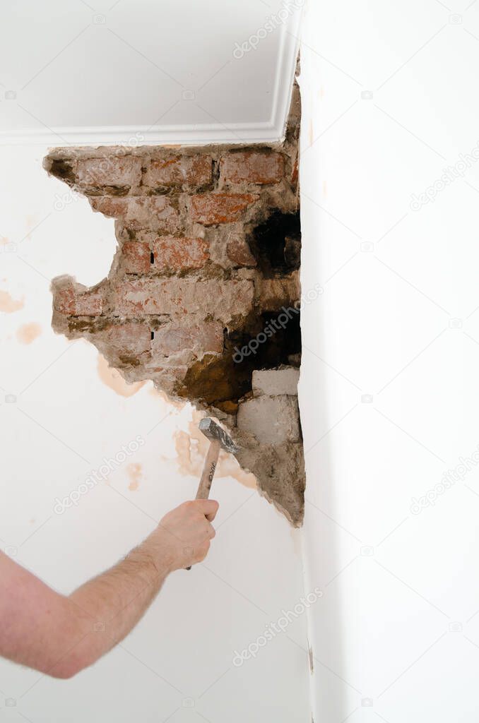 Worker man in white t shirt using hammer and destroy a wall at home, meaning heavy work. Mesh on split, close up shot