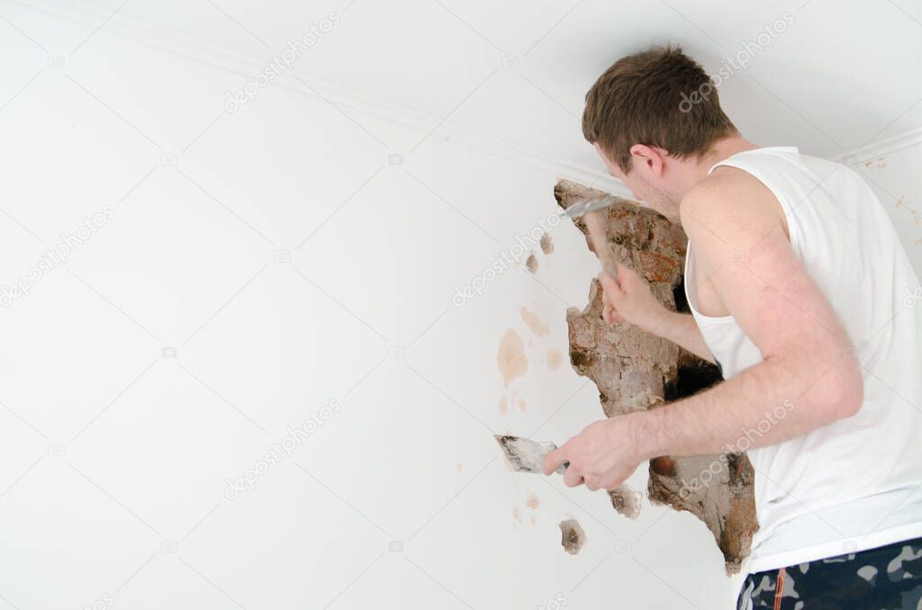 Worker man in white t shirt using hammer and destroy a wall at home, meaning heavy work. Mesh on split, close up shot