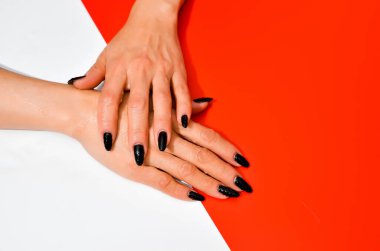 Modaya uygun siyah kadın manikürü. Güzel yaşlı kadının elleri beyaz ve kırmızı arka planda. Uzun tırnaklar