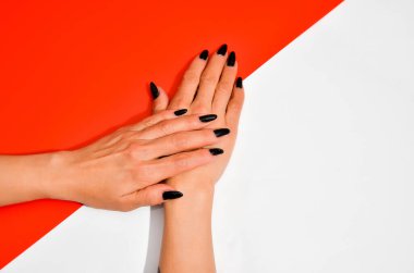 Modaya uygun siyah kadın manikürü. Güzel yaşlı kadının elleri beyaz ve kırmızı arka planda. Uzun tırnaklar