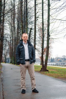 Mavi ceketli, bej pantolonlu yakışıklı bir işadamının fotoğrafı. Gülümsüyor ve kaldırımda yürüyor.