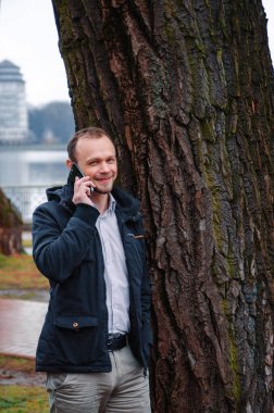 Mavi paltolu, bej pantolonlu yakışıklı bir işadamının gülümsemesi ve telefonda konuşması.