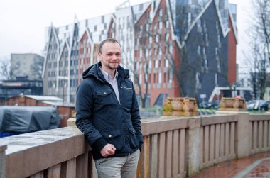 Mavi ceketli, bej pantolonlu yakışıklı bir işadamının fotoğrafı. Gülümsüyor ve kaldırımda yürüyor.