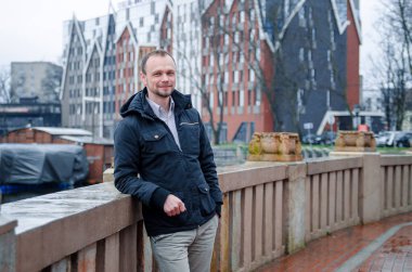 Mavi ceketli, bej pantolonlu yakışıklı bir işadamının fotoğrafı. Gülümsüyor ve kaldırımda yürüyor.