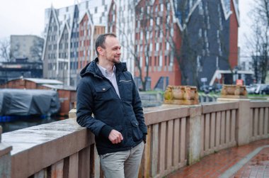 Mavi ceketli, bej pantolonlu yakışıklı bir işadamının fotoğrafı. Gülümsüyor ve kaldırımda yürüyor.