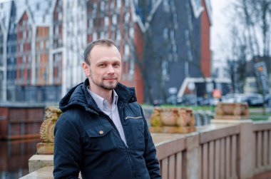 Mavi ceketli, bej pantolonlu yakışıklı bir işadamının fotoğrafı. Gülümsüyor ve kaldırımda yürüyor.