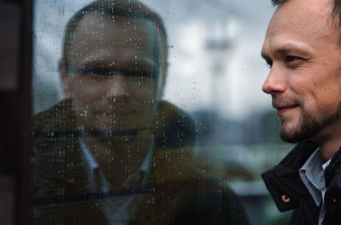 Yansımadaki yakışıklı bir adamın portresi. Koyu mavi ceketli gülümseyen adam.