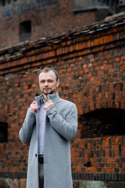 Gri paltolu ve biege pantolonlu yakışıklı işadamı gülümsüyor ve kaldırımda yürüyor.