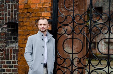 Gri paltolu ve biege pantolonlu yakışıklı işadamı gülümsüyor ve kaldırımda yürüyor.