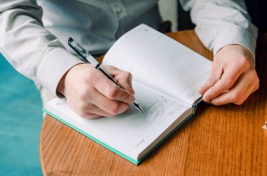 Yakışıklı işadamı gülümseyip deftere bir şeyler yazıyor. Masadaki kafede oturan adam.