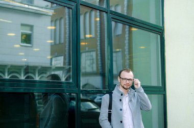 Gri paltolu ve biege pantolonlu yakışıklı işadamı gülümsüyor ve kaldırımda yürüyor.