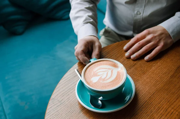 Ręce biznesmena wolnego strzelca z filiżanką kawy na stole. Niebieski kubek kawy z pianką i zdjęciem — Zdjęcie stockowe
