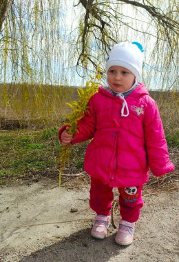 Küçük kız asfalt yolda duruyor ve güneşli bahar gününde ağaç dallarını tutuyor.