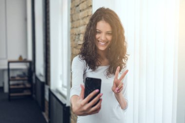 Portresi dikkatsiz oldukça büyüleyici emin neşeli neşeli sevimli sevimli kıvırcık kız alma selfie v-sign ile heyecanlı