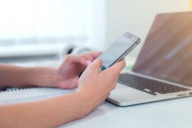 Modern akıllı telefon ile bilgisayar, onun cep telefonundan kısa mesaj yazarak işkadını ofisinde çalışırken kullanarak eller Close-up