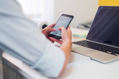 Modern akıllı telefon ile bilgisayar, onun cep telefonundan kısa mesaj yazarak işkadını ofisinde çalışırken kullanarak eller Close-up