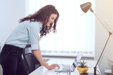 Mesaj yazma, bir dizüstü bilgisayar kullanarak ofisinde, duran güzel meşgul iş kadını,
